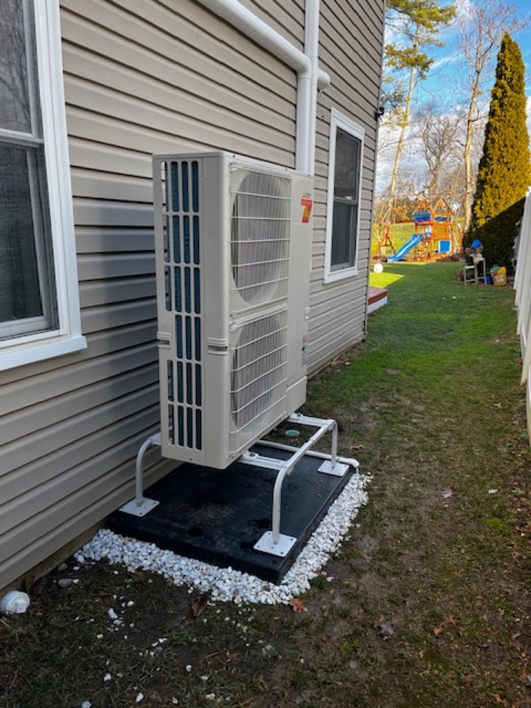 A Mitsubishi ductless outdoor unit installed on a pad beside a Connecticut home